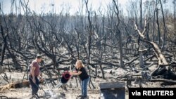 Hector Rivera and Wandi Blanco put water on hotspots on a neighbor's shed next to their home on Whitehead Boulevard after the Adkins Fire tore through the area in Panama City, Florida, U.S. March 5, 2022. 