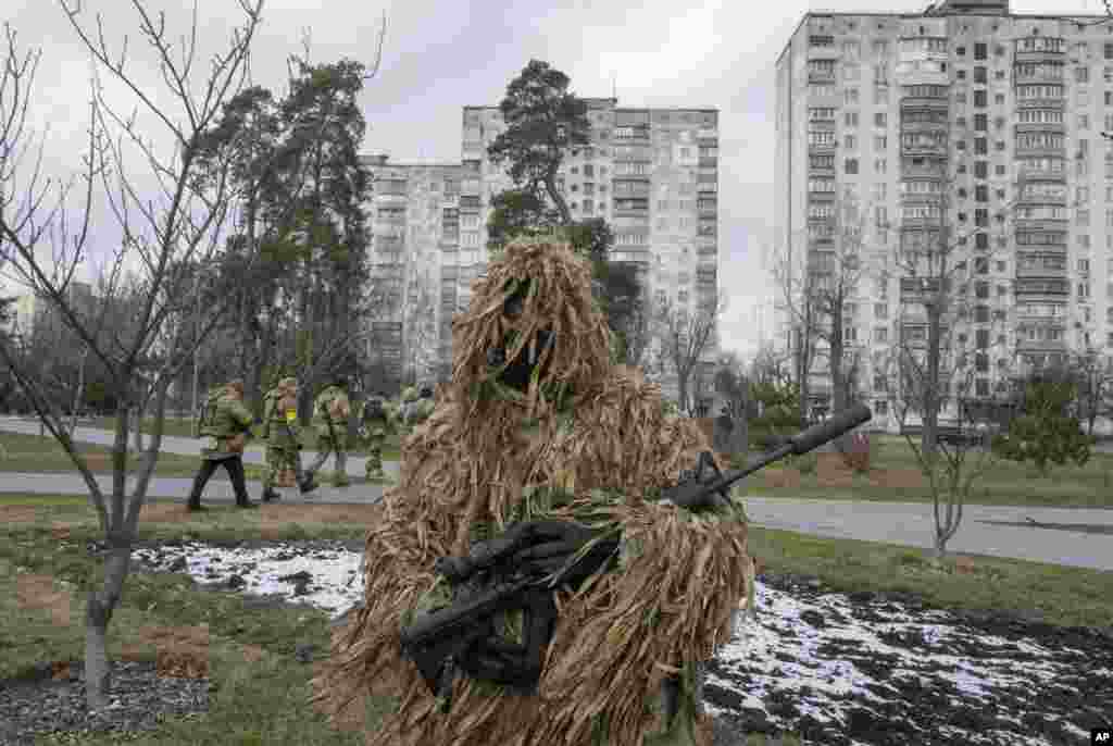 Ukrainian Territorial Defense Forces members walk past the city park as a camouflaged soldier stands in foreground, in the outskirts of Kyiv, March 9, 2022.