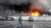 FILE - A Ukrainian serviceman walks past as fire and smoke rises over a damaged logistic center after shelling in Kyiv, Ukraine, March 3, 2022.