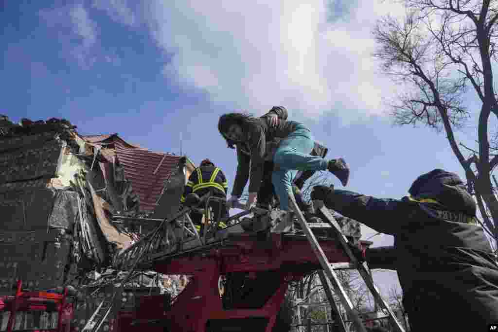 Firefighters help a woman to evacuate from a damaged by shelling apartment building in Mariupol, March 10, 2022.