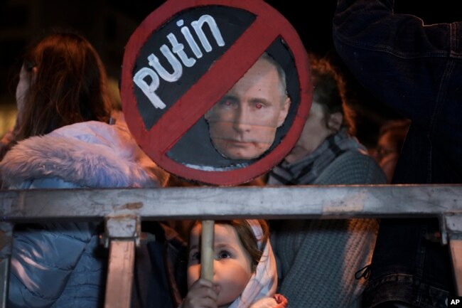 Seorang gadis memegang plakat bergambar Presiden Rusia Vladimir Putin pada protes terhadap invasi Rusia ke Ukraina di Tel Aviv, Israel, 5 Maret 2022. (Foto: AP)