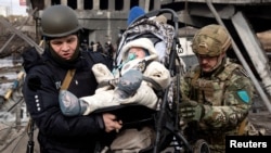 A baby is evacuated as people flee near a destroyed bridge to cross Irpin River as Russia's invasion on Ukraine continues, in Irpin outside Kyiv, March 9, 2022. 
