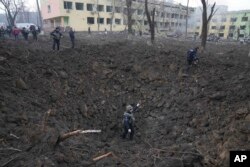 Ukrainian soldiers and emergency workers check a bomb crater outside a heavily damaged maternity hospital in Mariupol, Ukraine, March 9, 2022.