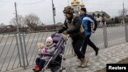 A service member of the Ukrainian armed forces helps to evacuate a child from the town of Irpin, on the only escape route used by locals after days of heavy shelling, while Russian troops advance towards the capital, in Irpin, near Kyiv, Ukraine, March 7, 2022.