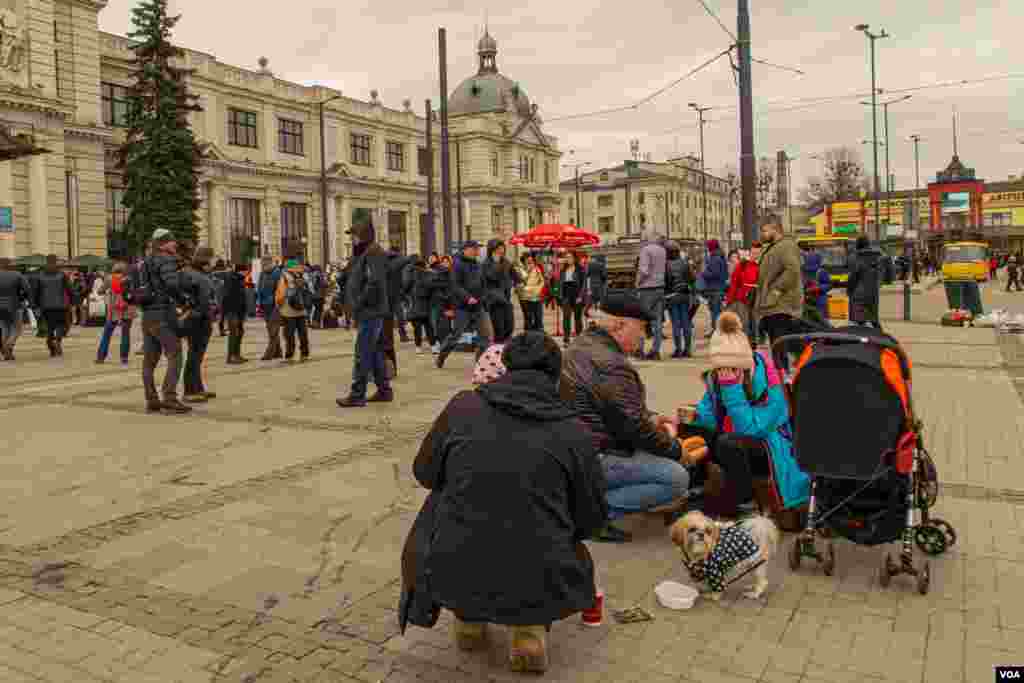 A grandfather tries to give some food to a girl at the Lviv main train station entrance on a cold afternoon, March 3, 2022. (VOA/Yan Boechat)