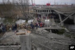 Orang-orang menyeberang di jalur improvisasi di bawah jembatan yang dihancurkan oleh serangan udara Rusia, saat melarikan diri dari kota Irpin di Ukraina, 5 Maret 2022. (Foto: AP)