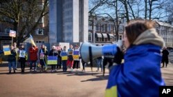 A woman is wrapped in the Ukrainian flag and shouts through a megaphone during a demonstration in front of the International Criminal Court in The Hague, Netherlands, March 7, 2022.
