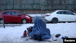 FILE - An Afghan woman holding her child begs on the snow-covered pavement in Kabul, Afghanistan, Jan. 27, 2022.