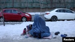 FILE - An Afghan woman holding her child begs on the snow-covered pavement in Kabul, Afghanistan, Jan. 27, 2022.