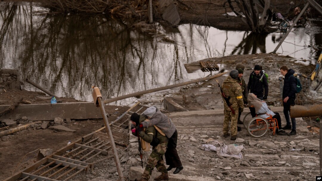 Seorang tentara Ukraina menggendong seorang perempuan lansia saat hendak menyeberangi sungai Irpin di pinggiran Kyiv, Ukraina, Senin, 7 Maret 2022. (AP/Emilio Morenatti)