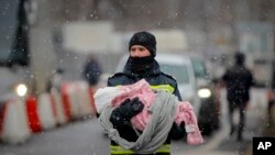 FILE - A firefighter holds the baby of a refugee fleeing the conflict from neighboring Ukraine at the Romanian-Ukrainian border, in Siret, Romania, March 7, 2022.