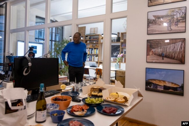 Burkinabe architect Diebedo Francis Kere is seen during a celebration next to pictures of some of his projects on the wall in his office in Berlin, on March 15, 2022, after being awarded the 2022 Pritzker Architecture Prize.