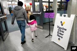 FILE - An information sign is displayed as a child arrives with her parent to receive the Pfizer COVID-19 vaccine for children 5- to 11-years-old at London Middle School in Wheeling, Ill., Nov. 17, 2021.