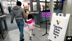 FILE - An information sign is displayed as a child arrives with her parent to receive the Pfizer COVID-19 vaccine for children 5- to 11-years-old at London Middle School in Wheeling, Ill., Nov. 17, 2021. 