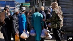 FILE - Afghans carry food supplies during a distribution of humanitarian aid for families in need, in Kabul, Afghanistan, Feb. 16, 2022.