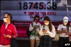 Orang-orang berdiri di depan layar yang menunjukkan Indeks Hang Seng di Hong Kong pada 15 Maret 2022. (Foto: DALE DE LA REY/AFP)