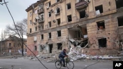 A man rides a bicycle in front of an apartment building damaged by shelling in Mariupol, Ukraine, March 9, 2022.