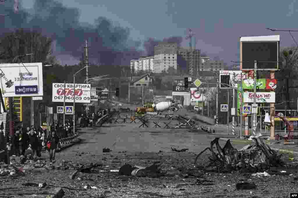 Residents walk past a body lying in the middle of a road as they evacuate the city of Irpin, north of Kyiv, March 10, 2022. Kyiv&#39;s northwest suburbs such as Irpin and Bucha have been enduring shellfire and bombardments for more than a week, prompting a mass evacuation effort.