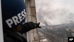 El fotógrafo de Associated Press Evgeniy Maloletka señala el humo que se eleva después de un ataque aéreo en un hospital de maternidad, en Mariupol, Ucrania, el miércoles 9 de marzo de 2022. [Foto AP/Mstyslav Chernov]