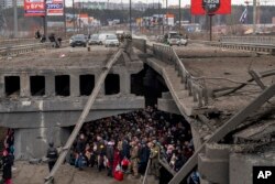 Warga Ukraina berkerumun di bawah jembatan yang hancur saat mereka mencoba melarikan diri melintasi Sungai Irpin di pinggiran Kyiv, Ukraina, Sabtu, 5 Maret 2022. (Foto: AP/Emilio Morenatti)