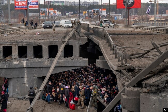 Warga Ukraina berkerumun di bawah jembatan yang hancur saat mereka mencoba melarikan diri melintasi Sungai Irpin di pinggiran Kyiv, Ukraina, Sabtu, 5 Maret 2022. (Foto: AP/Emilio Morenatti)