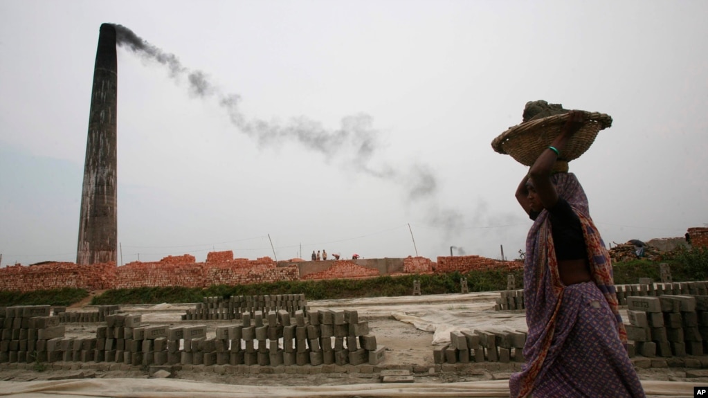 FILE: Smoke emits from chimney as a Bangladeshi female worker carries clay at a brick field at Amin Bazar, outskirts of Dhaka, Bangladesh, Thursday, May 14, 2009.