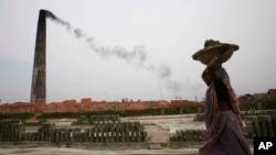 FILE - Smoke emits from chimney as a Bangladeshi female worker carries clay at a brick field at Amin Bazar, outskirts of Dhaka, Bangladesh, Thursday, May 14, 2009.