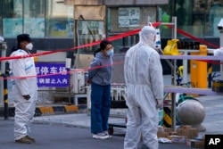 Security guards wearing protective suits stand watch as a masked woman waits for her parcel at a residential building locked down for health monitoring following a COVID-19 case detected in the area, in Beijing, March 28, 2022.