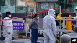 Security guards wearing protective suits stand watch as a masked woman waits for her parcel at a residential building locked down for health monitoring following a COVID-19 case detected in the area, in Beijing, March 28, 2022. 