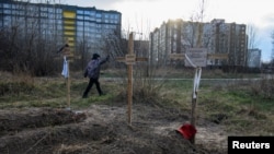 2022年4月4日，在乌克兰基辅地区的布查，一名男孩走过葬有平民尸体的坟墓。据当地居民称，这些平民是被俄罗斯士兵杀害的。（路透社）