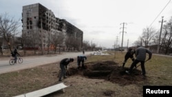 20일 우크라이나 남동부 항구도시 마리우폴 시민들이 도로변에 폭격 희생자를 매장하고 있다.