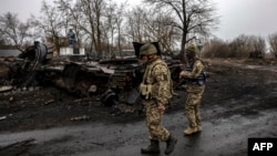 Ukrainian soldiers patrol next to a destroyed Russian tank in the village of Lukianivka near Kyiv on March 30, 2022.
