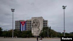 La gente camina en la plaza de la Revolución cerca de una imagen del difunto revolucionario Ernesto 'Che' Guevara en medio de preocupaciones por la propagación del brote de la enfermedad coronavirus, en La Habana, el 1 de mayo de 2020.