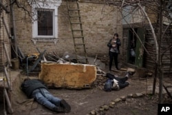 Žena hoda pored tijela svog muža, brata i još jednog muškarca, koji su ubijeni ispred njene kuće u Buči, na periferiji Kijeva, Ukrajina, u ponedjeljak, 4. aprila 2022.