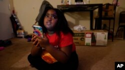 Brooklynn Chiles, 8, glances up from her smartphone at home where she lives with her mother, Danielle Mitchell in Washington, Jan. 9, 2022. 