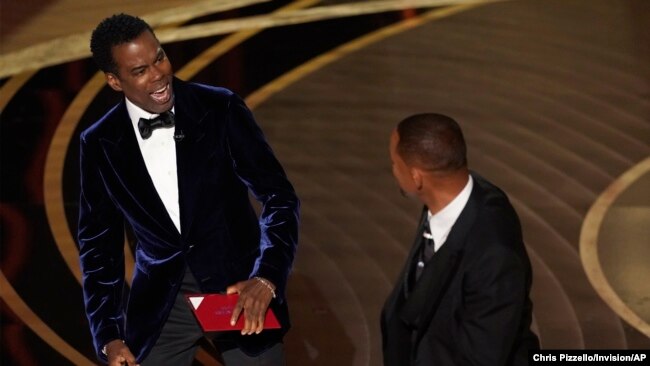 Presenter Chris Rock, left, reacts after being hit on stage by Will Smith while presenting the award for best documentary feature at the Oscars on Sunday, March 27, 2022