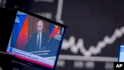 На фото: президент Росії Володимир Путін на телевізійному екрані на фондовій бріжі у Франкфурті, Німеччина. 25 лютого, 2022. Текст на екрані : "Війна пропаганди онлайн та на ТБ".