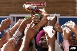 Seorang pengunjung membagikan minuman keras setelah membawa prasad (sesajen miras) tersebut ke kuil Baba Rode Shah di desa Bhoma, sekitar 35 kilometer dari Amritsar, 24 Maret 2022. (Narinder NANU / AFP)