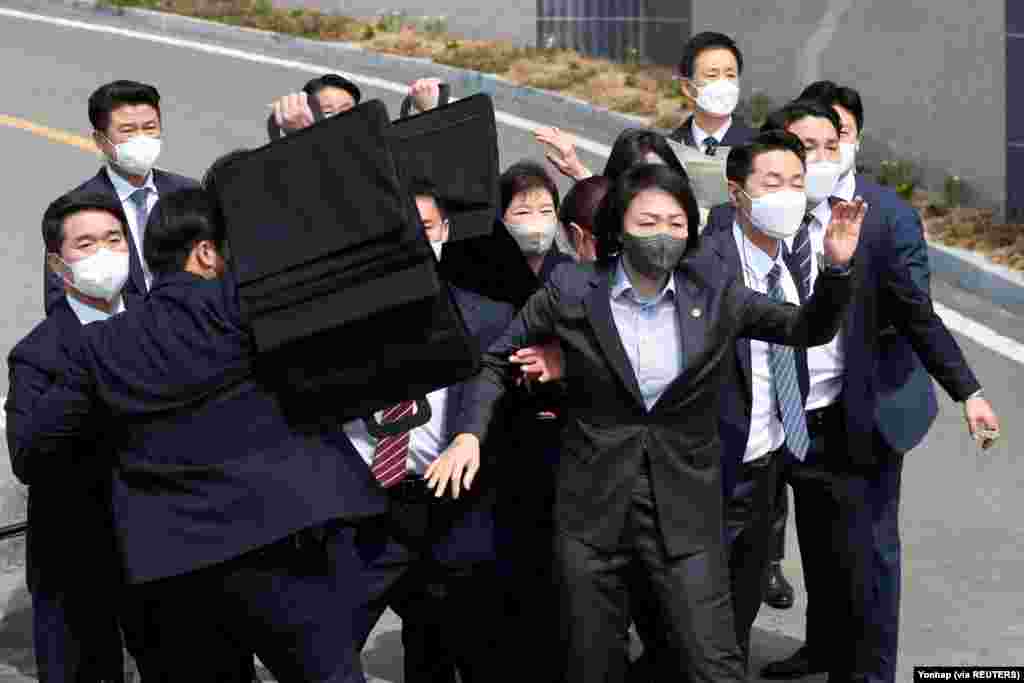 Bodyguards surround former South Korean President Park Geun-hye (in center rear wearing a white mask) as an unidentified man throws a glass bottle (not pictured) at her in front of her home in Daegu.