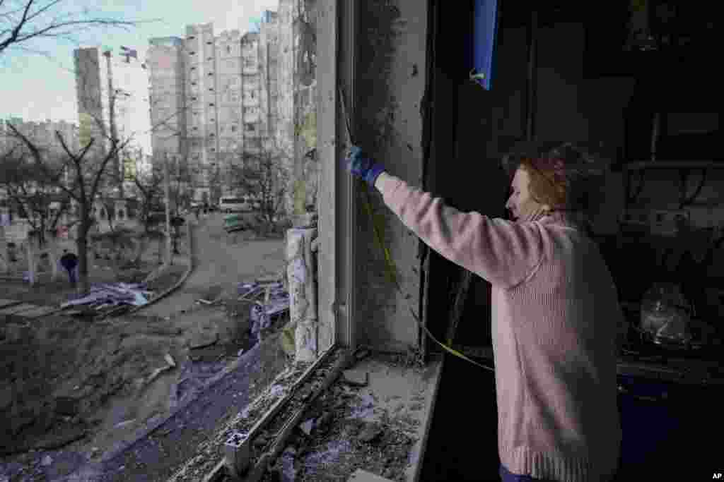 Una mujer mide una ventana antes de cubrirla con láminas de plástico en un edificio dañado por un bombardeo el día anterior en Kiev, Ucrania, el lunes 21 de marzo de 2022. (AP Photo/Vadim Ghirda).