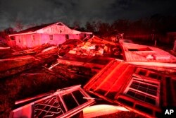 Rumah-rumah yang hancur, diterangi lampu mobil pemadam kebakaran, terlihat setelah tornado melanda kawasan Arabi, Louisiana., Selasa, 22 Maret 2022. (AP/Gerald Herbert)