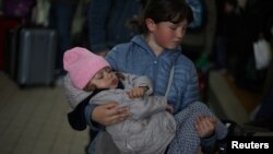 Ukrainian refugees Tania, 2, and Galina, 11, wait in the ticket hall at Przemysl Glowny train station, after fleeing the Russian invasion of Ukraine, in Poland.
