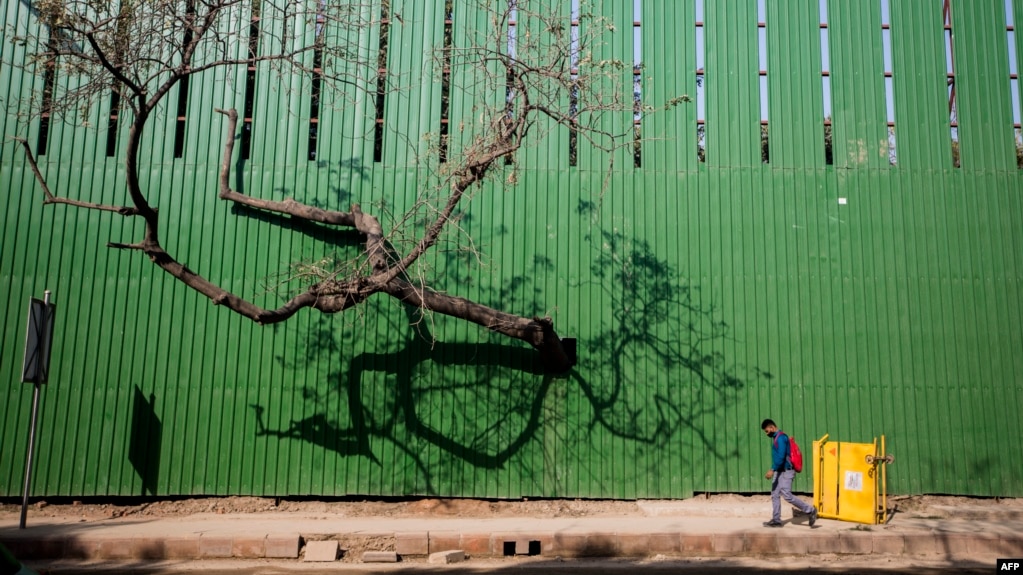 A man walks past a fence of a construction site along a street in New Delhi, India, March 9, 2022.