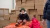 A Ukrainian child eats a slice of bread sitting in a storage facility on sacks of onions as another one plays. Psychiatrists worry about the long-term health effects of the war on Ukraine’s youngsters (Jamie Dettmer/VOA) 