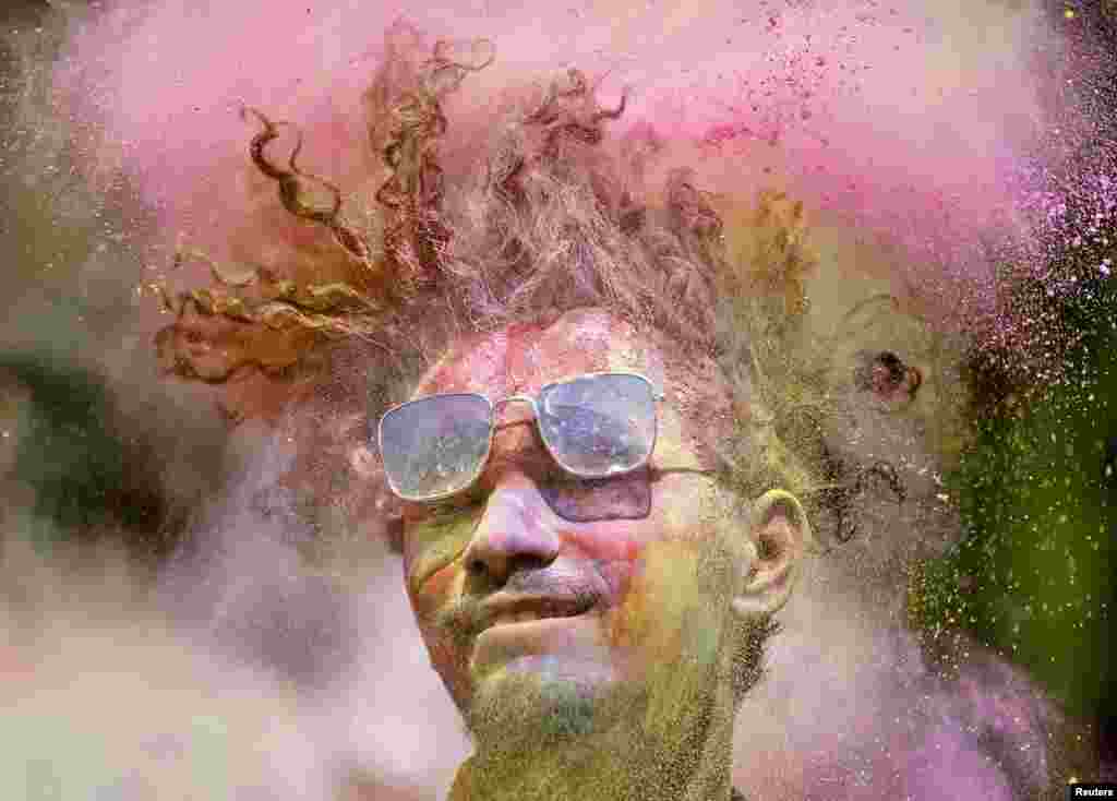 A man covered in colored powder shakes his head during Holi celebrations in Ahmedabad, India.