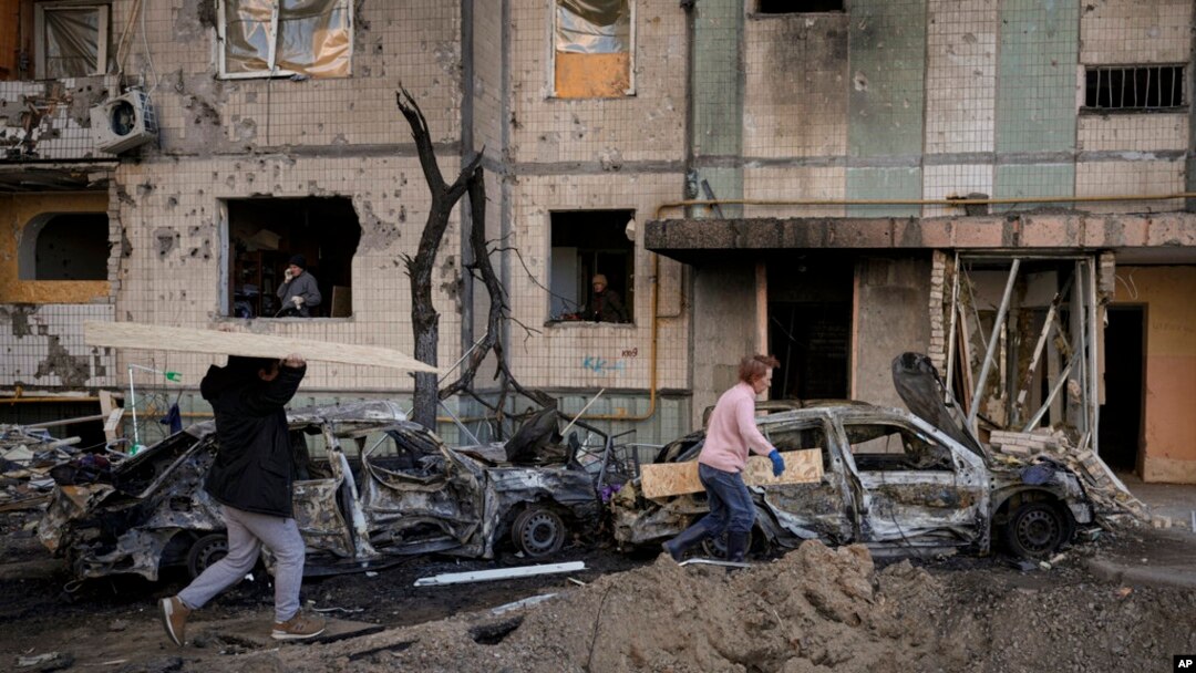 Gente carga tablones para cubrir las ventanas de un edificio dañado por una bomba el día anterior en Kiev, Ucrania, el lunes 21 de marzo de 2022. 