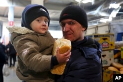 A man and his child wait to get food and drinking water at a supermarket in the territory under the Government of the Donetsk People's Republic control, on the outskirts of Mariupol, Ukraine, March 24, 2022.