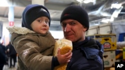 A man and his child wait to get food and drinking water at a supermarket in the territory under the Government of the Donetsk People's Republic control, on the outskirts of Mariupol, Ukraine, March 24, 2022. 