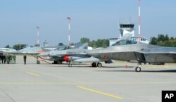 FILE - Officials walk past fighter jets, including a Polish Air Force MIG-29, left, at a military base in Lask, Poland, Aug. 31, 2015.