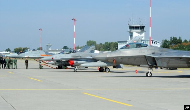 FILE - Officials walk past fighter jets, including a Polish Air Force MIG-29, left, at a military base in Lask, Poland, Aug. 31, 2015.